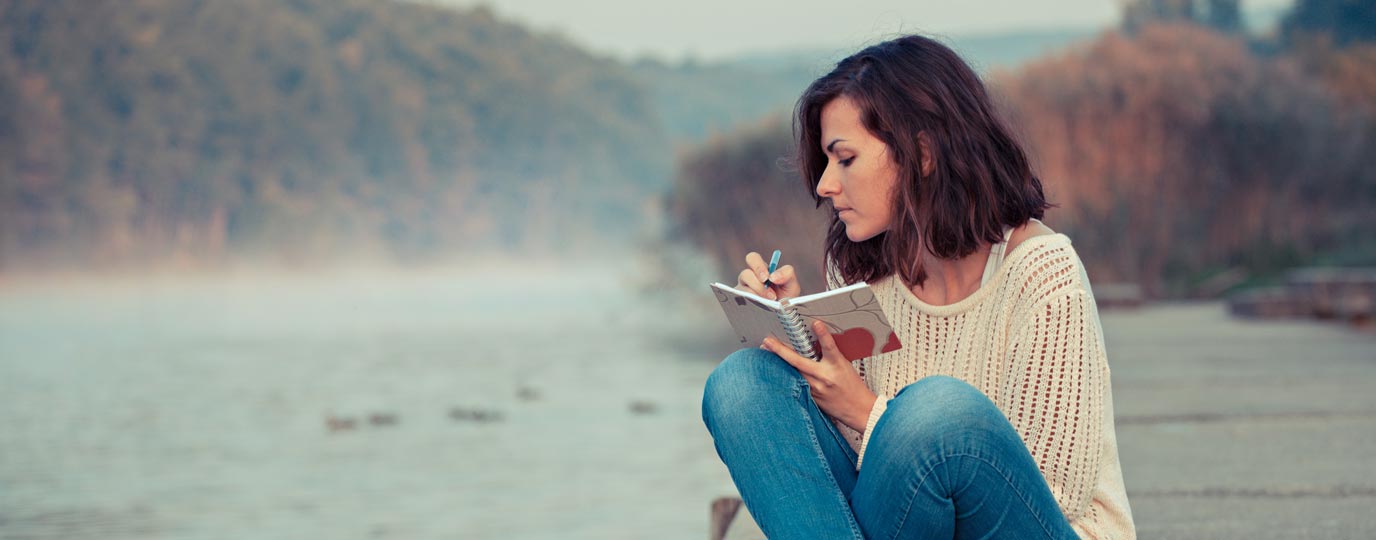 Woman sitting on a jetty writing in a notepad