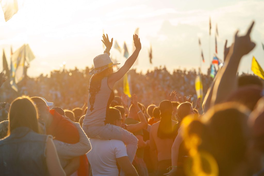 Glastonbury Festival - sustainable festivals, girl on shoulders in sunset