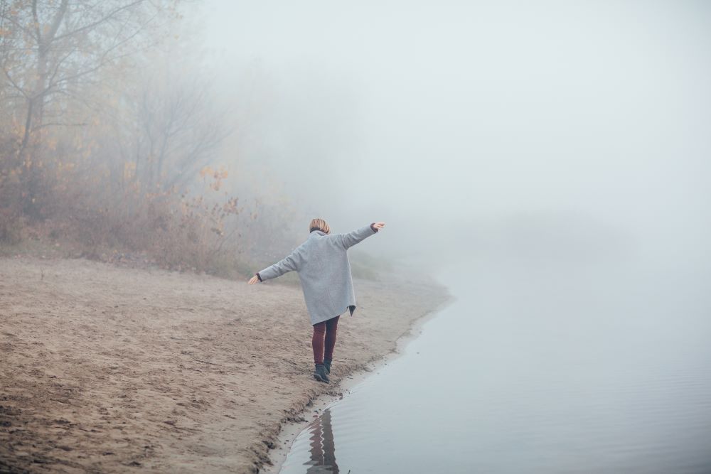 a woman walking beside a lake on a cold day