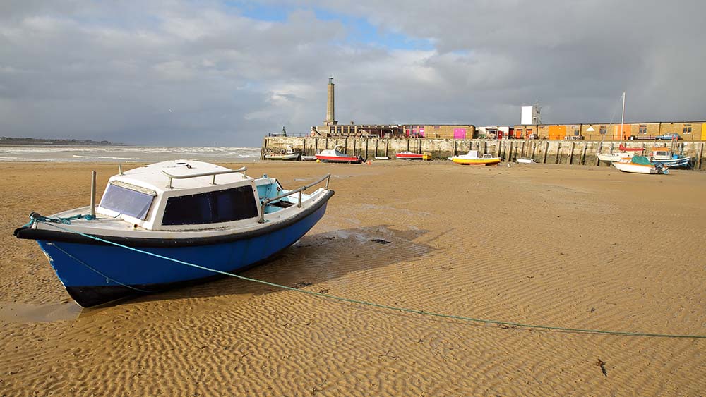 The beach at low tide with mooring boats and Margate Harbor Arm