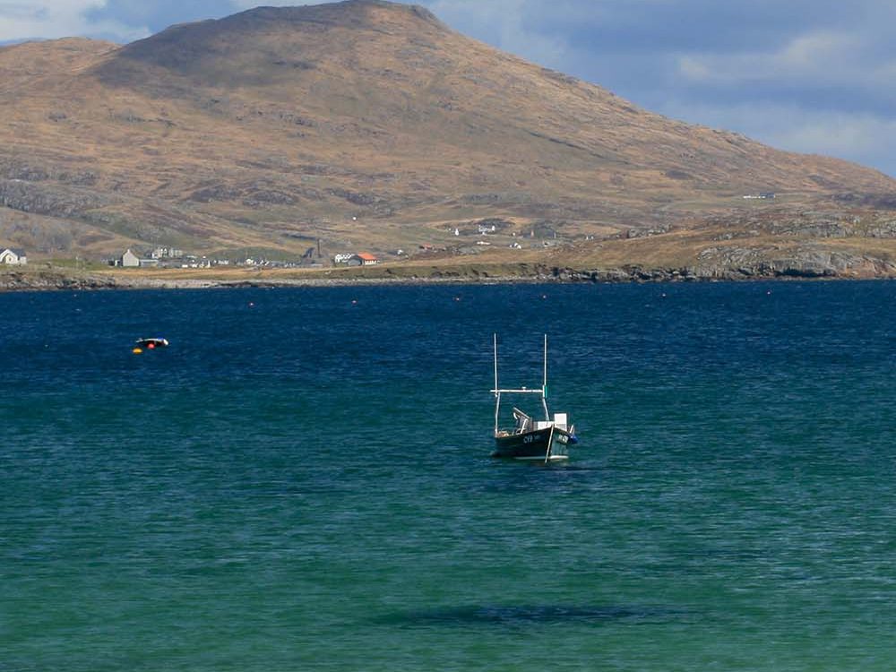 Vatersay - a boat on the sea with a mountain behind