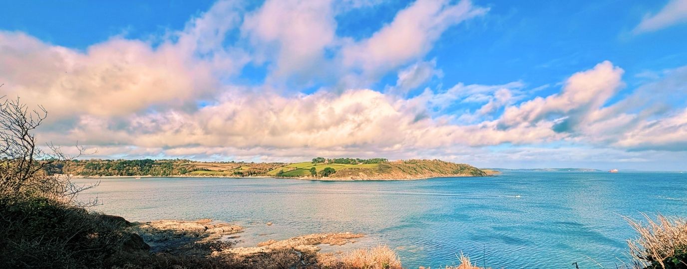 Scenic view of a calm coastal landscape with rolling hills and a blue sky dotted with clouds.