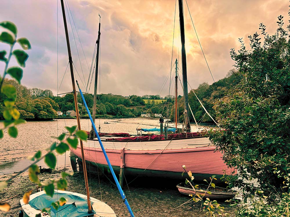 A picturesque scene of boats moored by a river, surrounded by lush greenery and a cloudy sky at sunset.