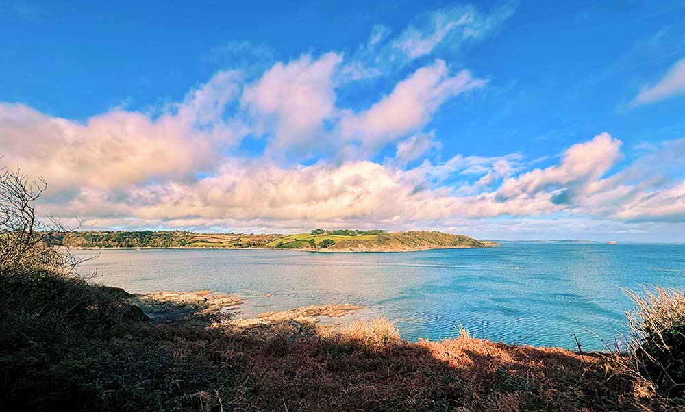 Scenic view of a calm coastal landscape with rolling hills and a blue sky dotted with clouds.