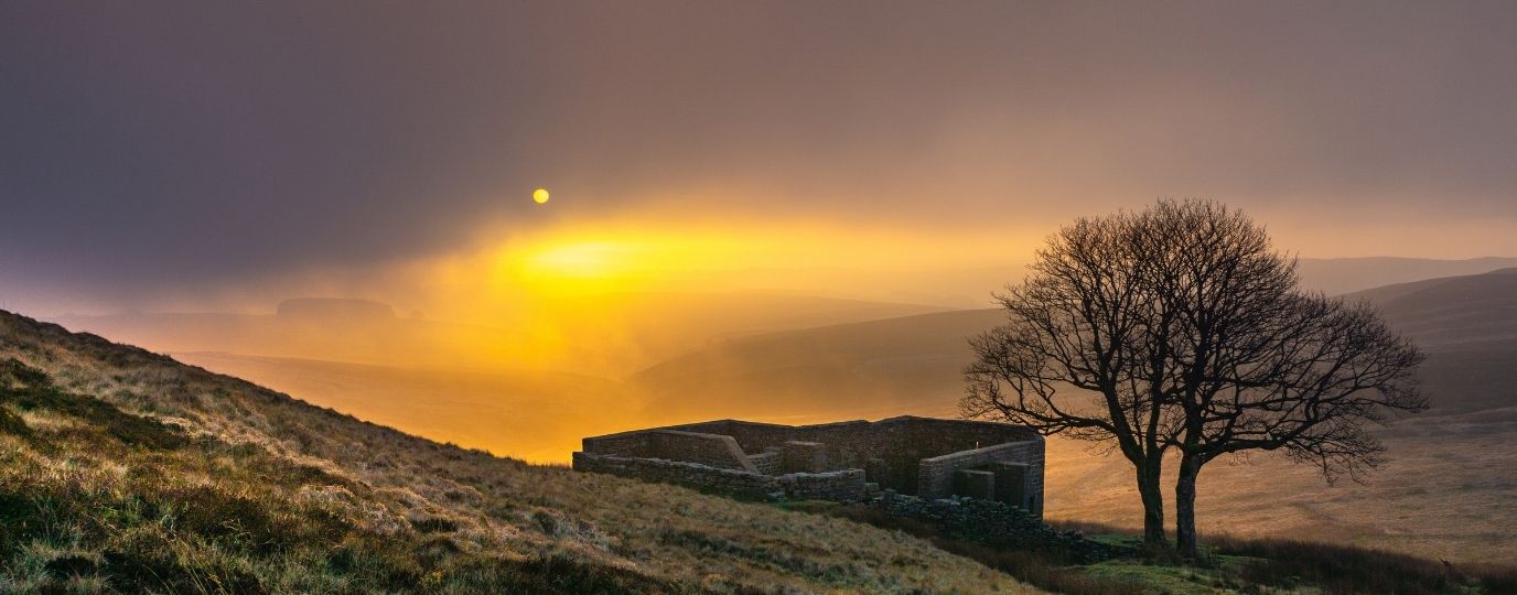 an old cottage and the sun setting behind